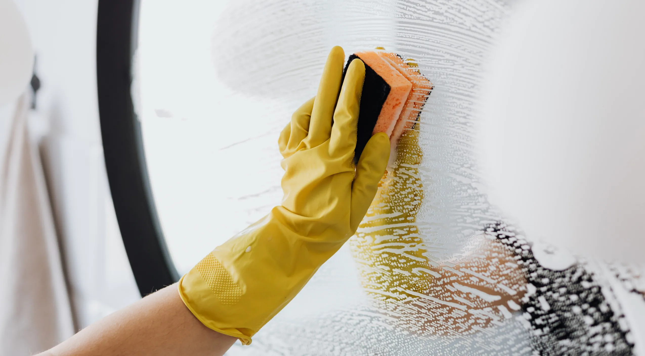 Reinigungskraft mit gelben Handschuhen putzt eine Glasfläche im Badezimmer für streifenfreie Sauberkeit.